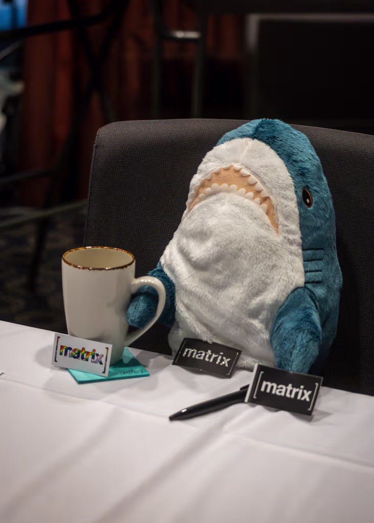 A Blåhaj is staffing the Foundation booth, holding a cup of coffee in its right flipper.